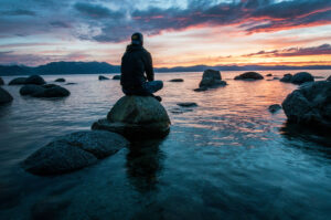 man sitting on a rock in the ocean at sunrise